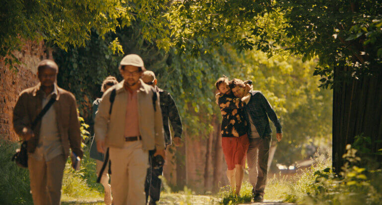 Kurt Egyiawan, Will Sharpe walking in a park as Kieran Culkin and Jesse Eisenberg walk in an embrace.